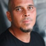 Man with goatee in blackshirt in grey doorway