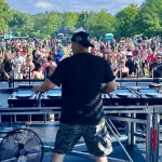 DJ on outdoor festival stage with crowd beyond in daylight